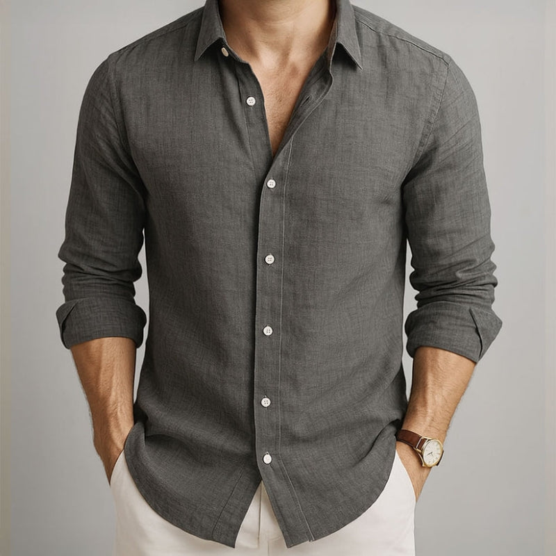 Man wearing a gray button-up shirt with rolled-up sleeves on a neutral background and beige linen pants