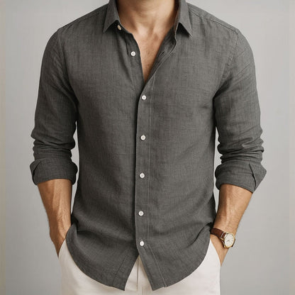 Man wearing a gray button-up shirt with rolled-up sleeves on a neutral background and beige linen pants